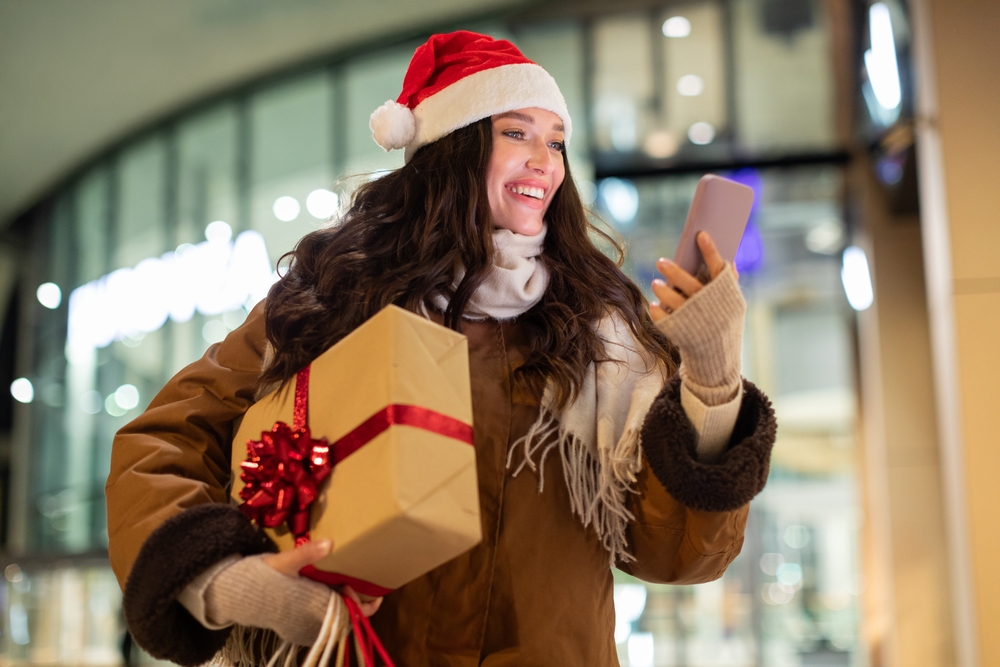 Excited,Smiling,Woman,In,Santa,Hat,Walking,Near,Mall,In